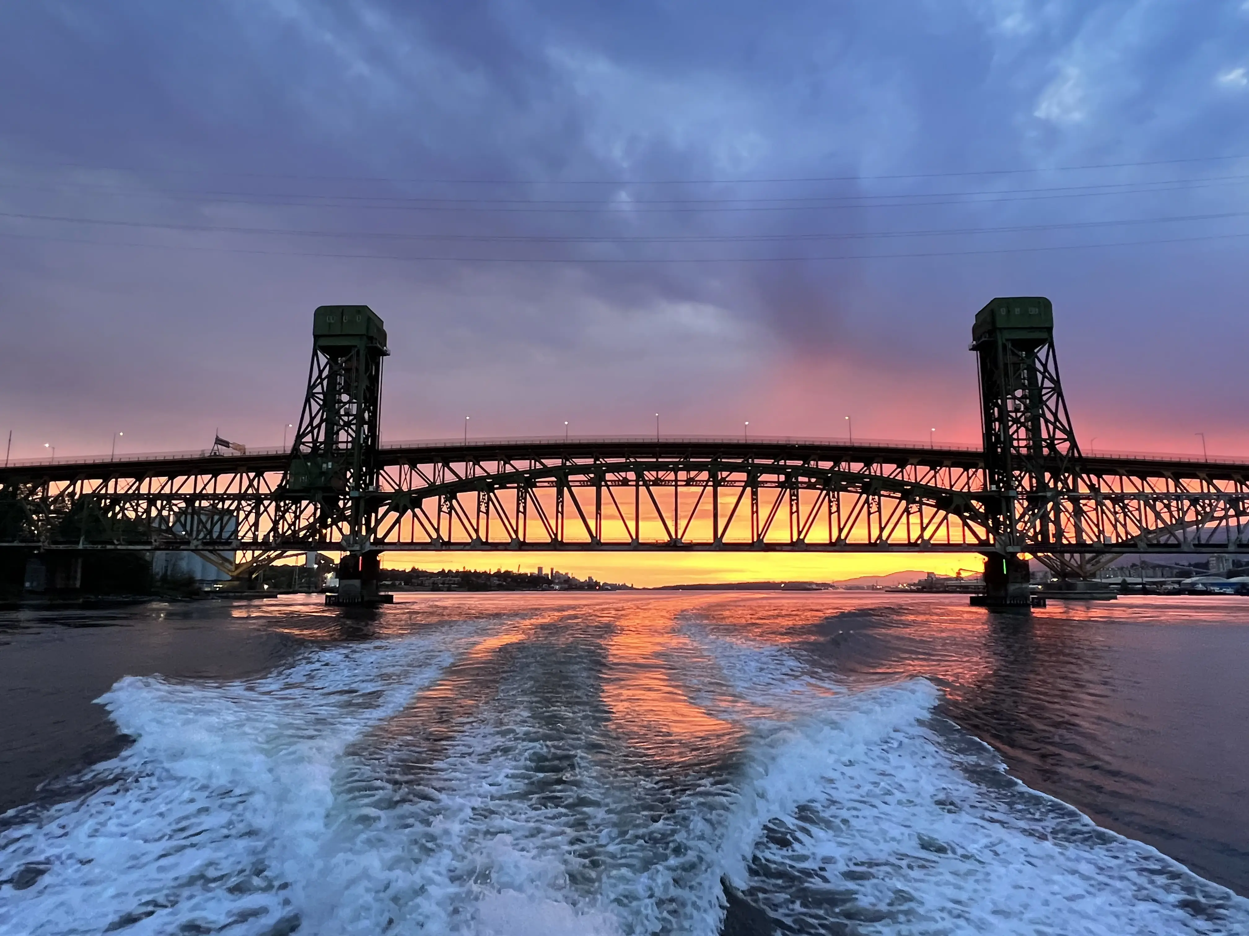 Golden sunset glowing beneath a bridge, seen from the wake of a yacht